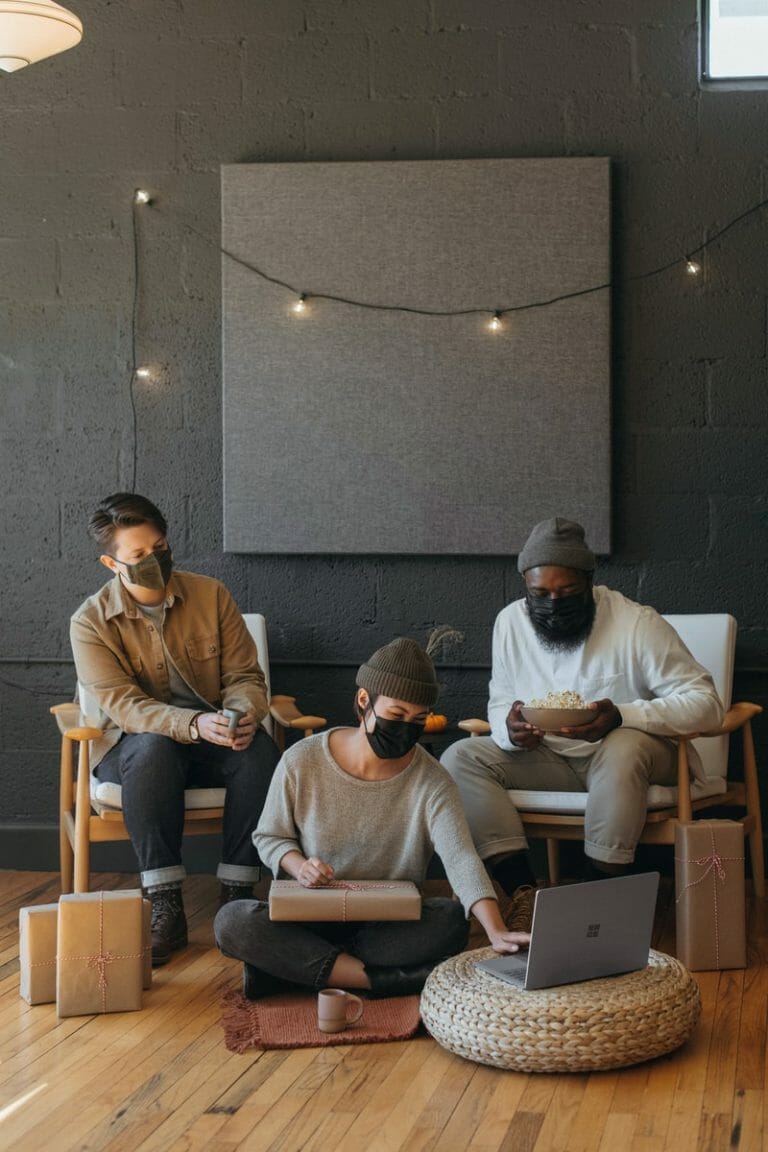 Three coworkers wearing masks on a Surface laptop with Christmas presents on a cart